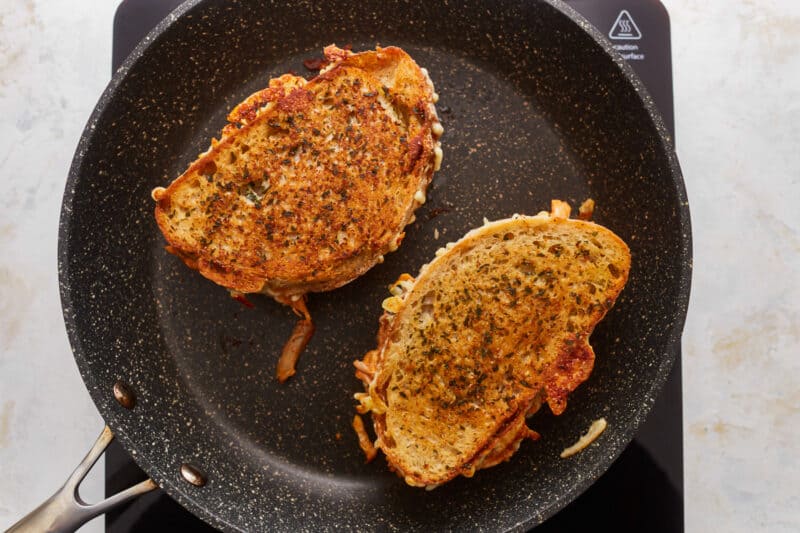 Two grilled sandwiches in a pan on a stovetop.