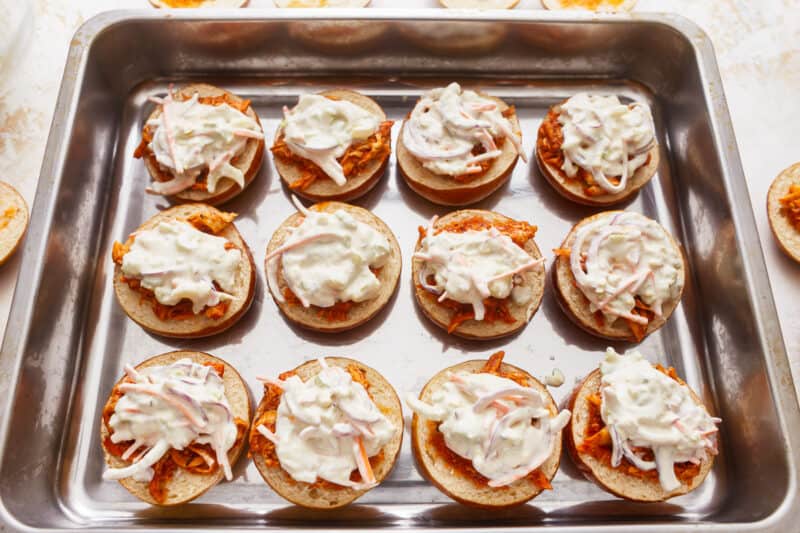 A tray full of chicken sandwiches with sour cream on top.