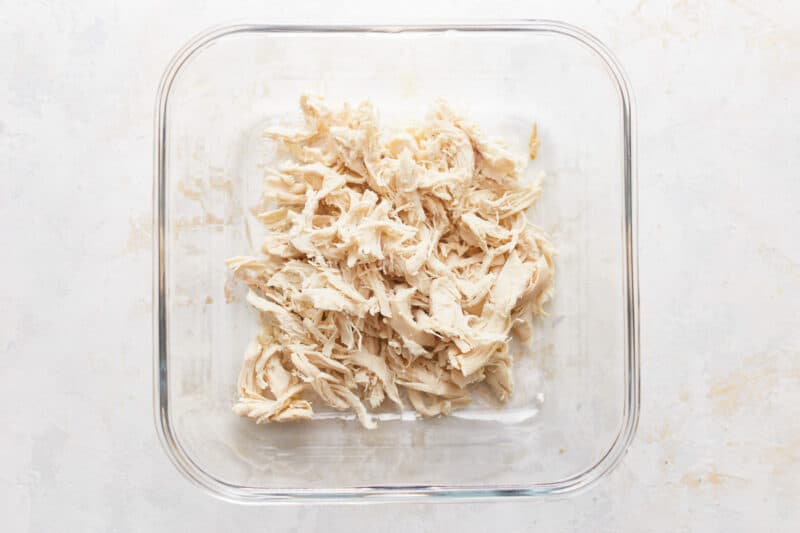 Shredded chicken in a glass dish on a white background.