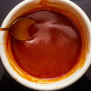 A cup of sauce with a spoon in it.