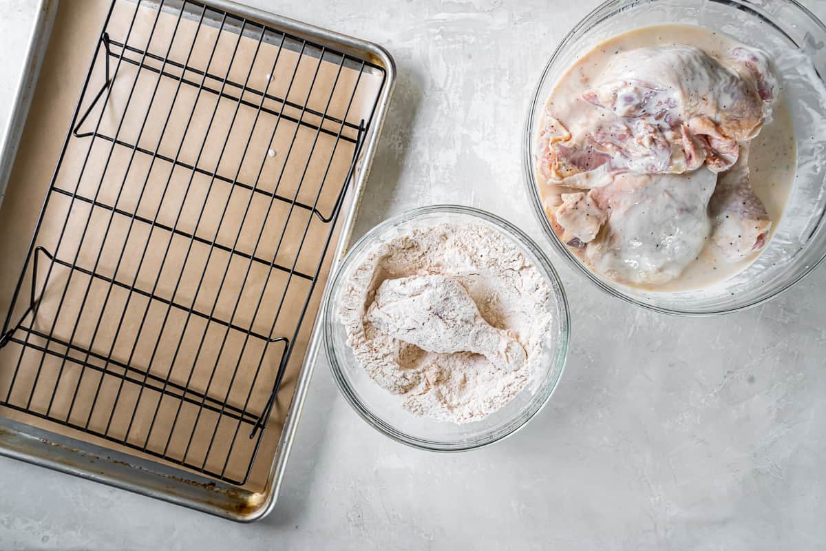 A baking sheet with a tray of chicken and a bowl of flour.