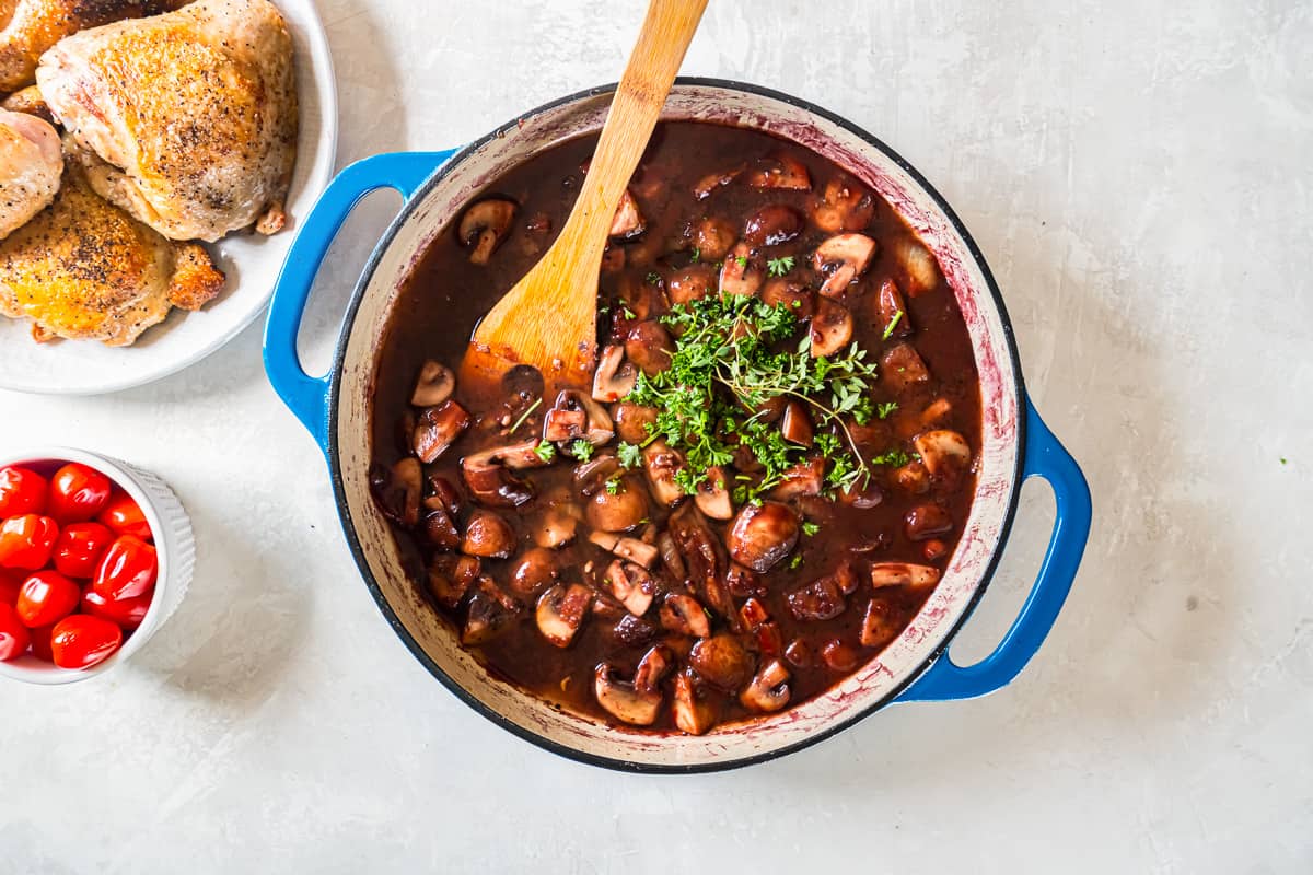 A pot of stew with mushrooms, tomatoes, and a wooden spoon.