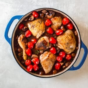 Roasted chicken with mushrooms and tomatoes in a blue pan.