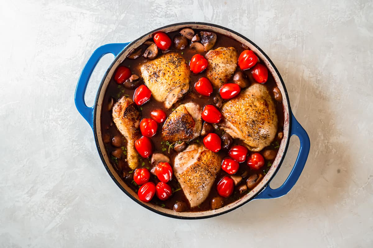 Roasted chicken with mushrooms and tomatoes in a blue pan.