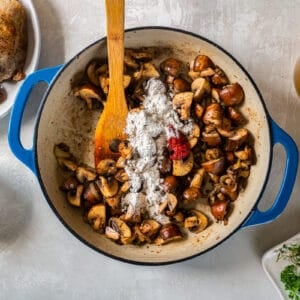 A pan with mushrooms, tomatoes, and a wooden spoon.