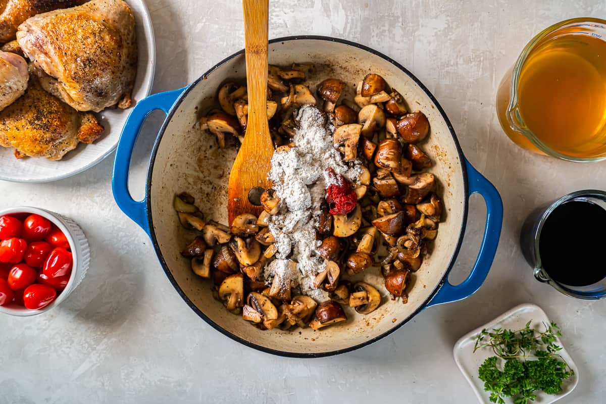 A pan with mushrooms, tomatoes, and a wooden spoon.