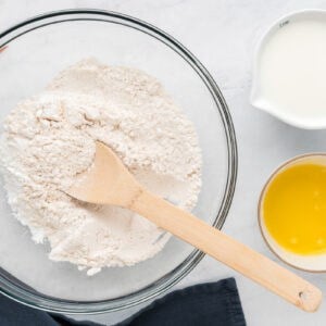 A bowl of flour, eggs and a wooden spoon on a marble table.