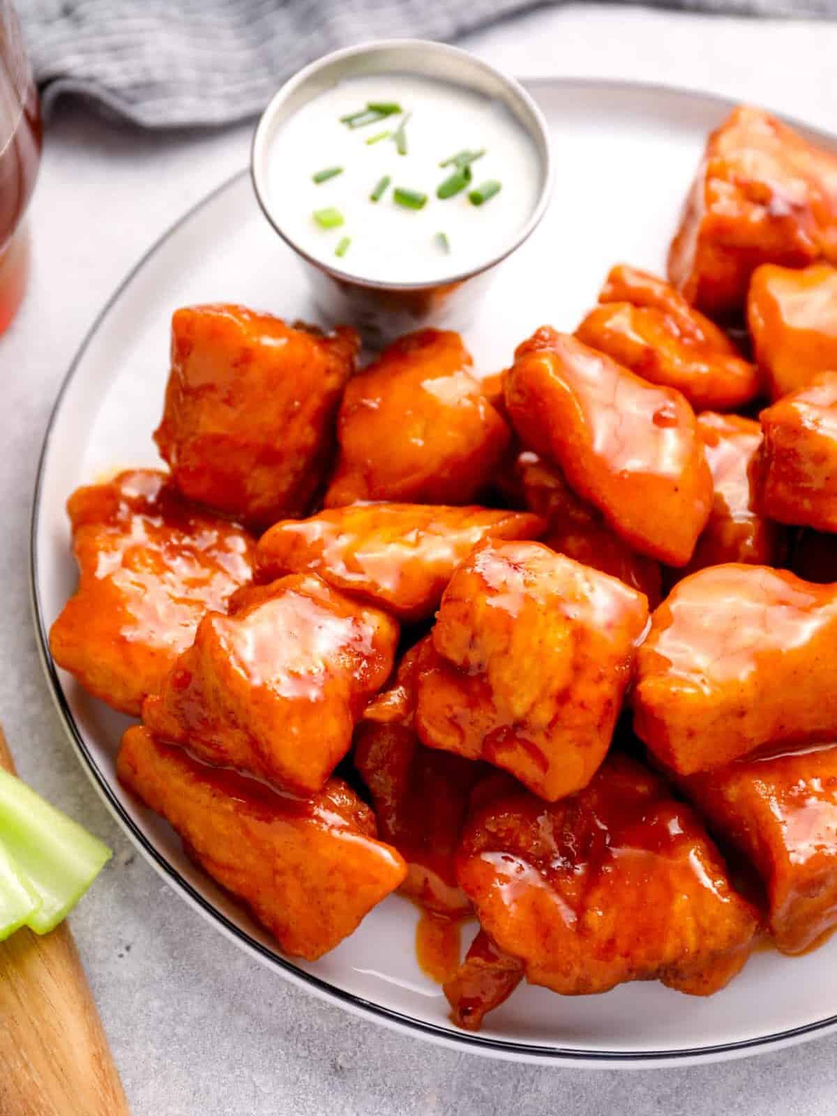 a plate of boneless chicken wings covered in buffalo sauce.