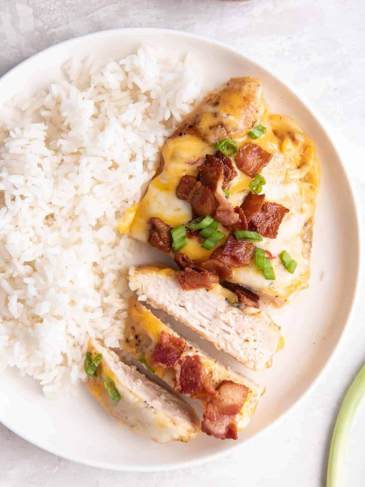 close up overhead view of a sliced cheesy bacon ranch chicken breast on a white plate with rice.