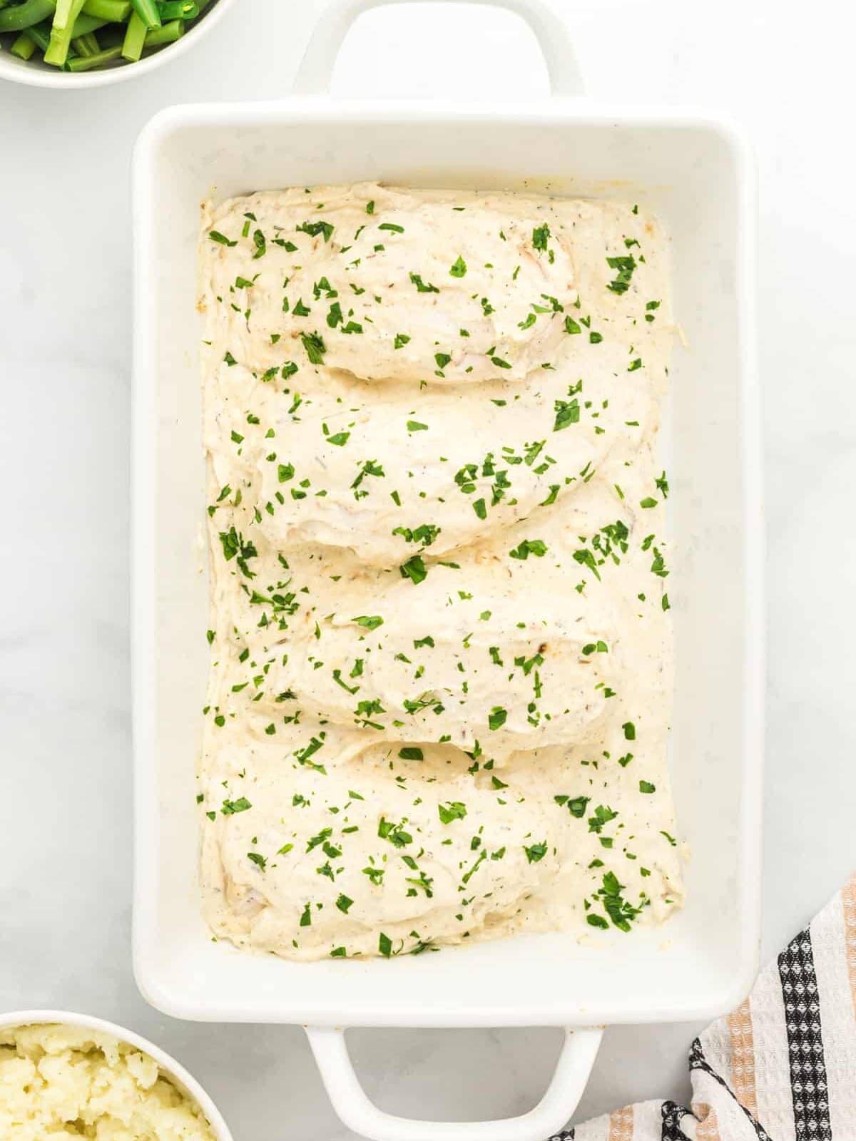 overhead view of creamy herb chicken in a white baking pan.