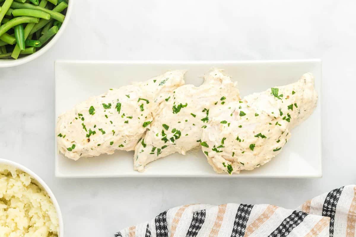 overhead view of creamy herb chicken on a white serving plate.