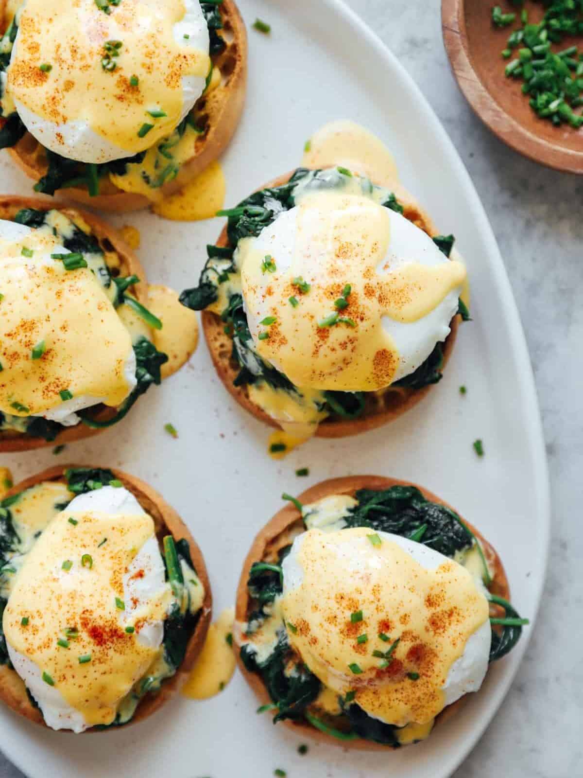 overhead view of 5 eggs florentine benedicts on a white serving tray.