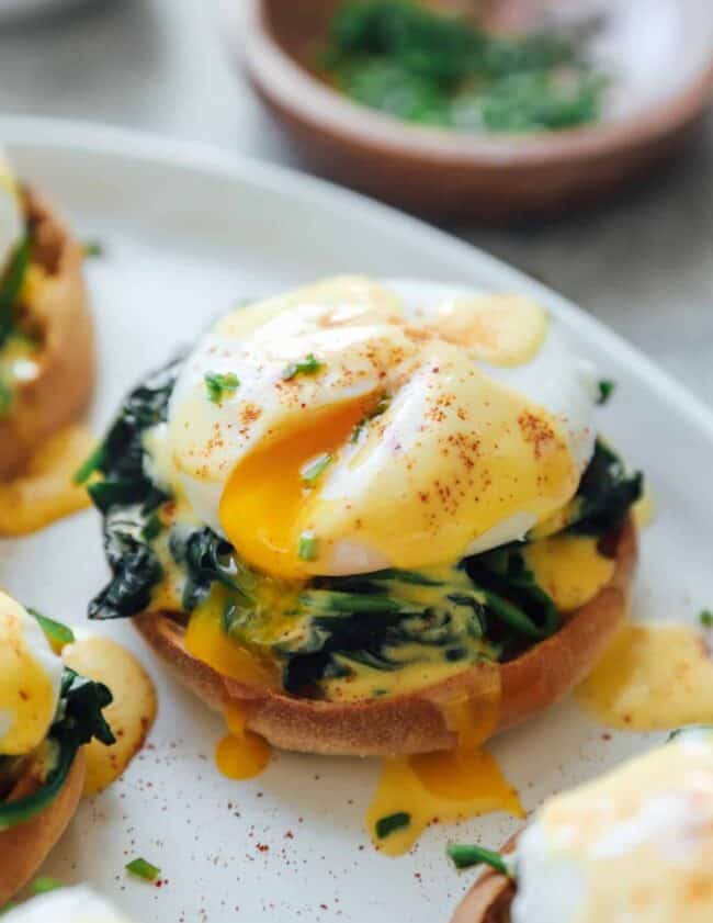 three-quarters view of eggs florentine benedict on a white serving tray with the yolk spilling out.