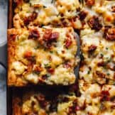 a slice of crescent roll breakfast pizza being lifted from a sheet pan by a spatula.