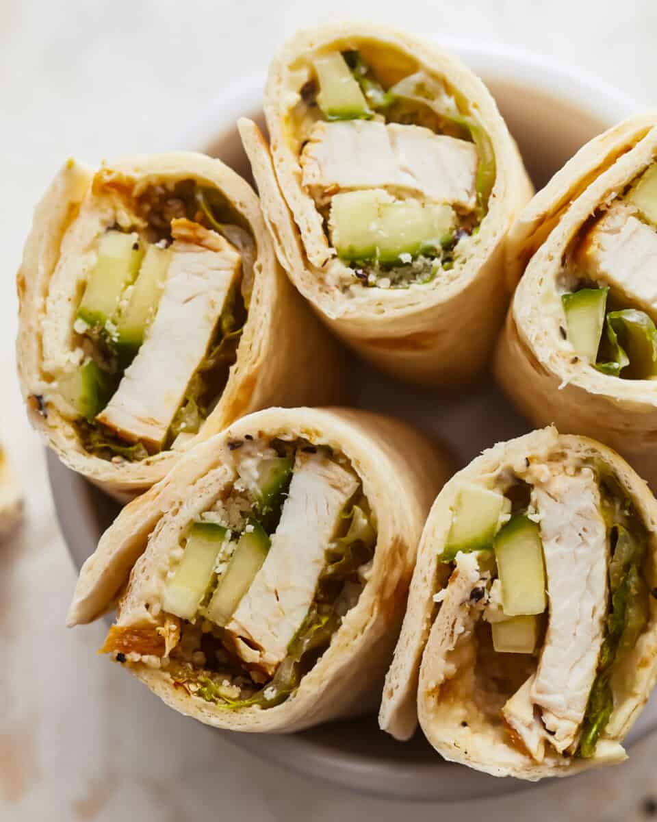 Chicken and cucumber wraps in a white bowl.