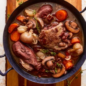 A pot of stew with meat and vegetables on a wooden cutting board.