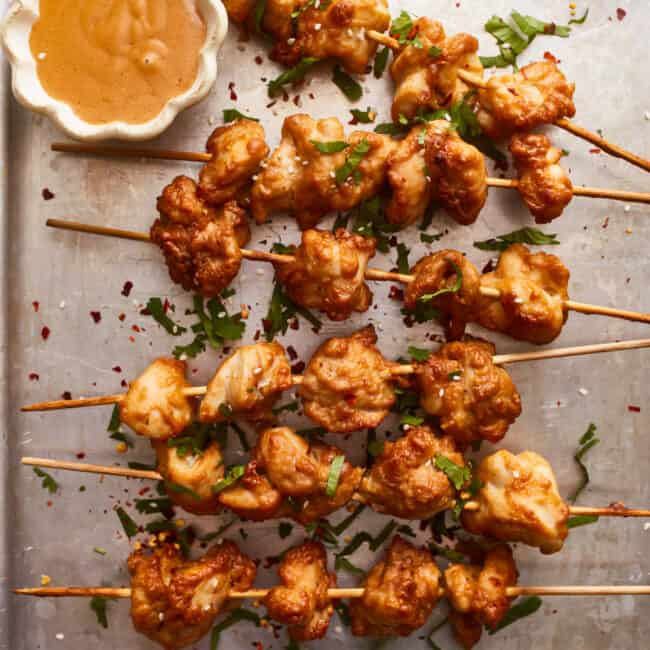 Chicken skewers with dipping sauce on a tray.