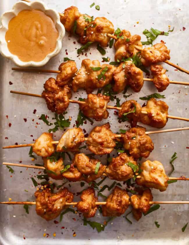 Chicken skewers with dipping sauce on a tray.