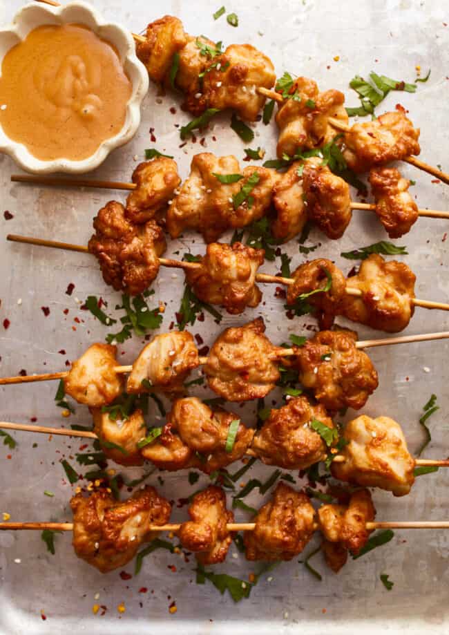Chicken skewers with dipping sauce on a tray.