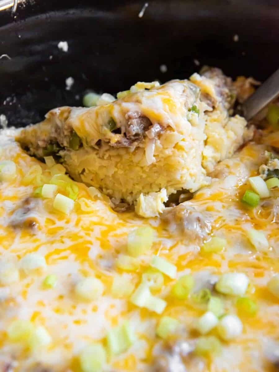 a piece of crock pot casserole with cheese and green onions.