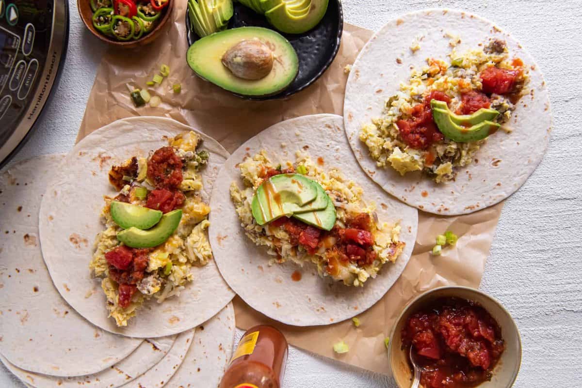 unwrapped breakfast burritos laid flat on a tabletop, surrounded by ingredients