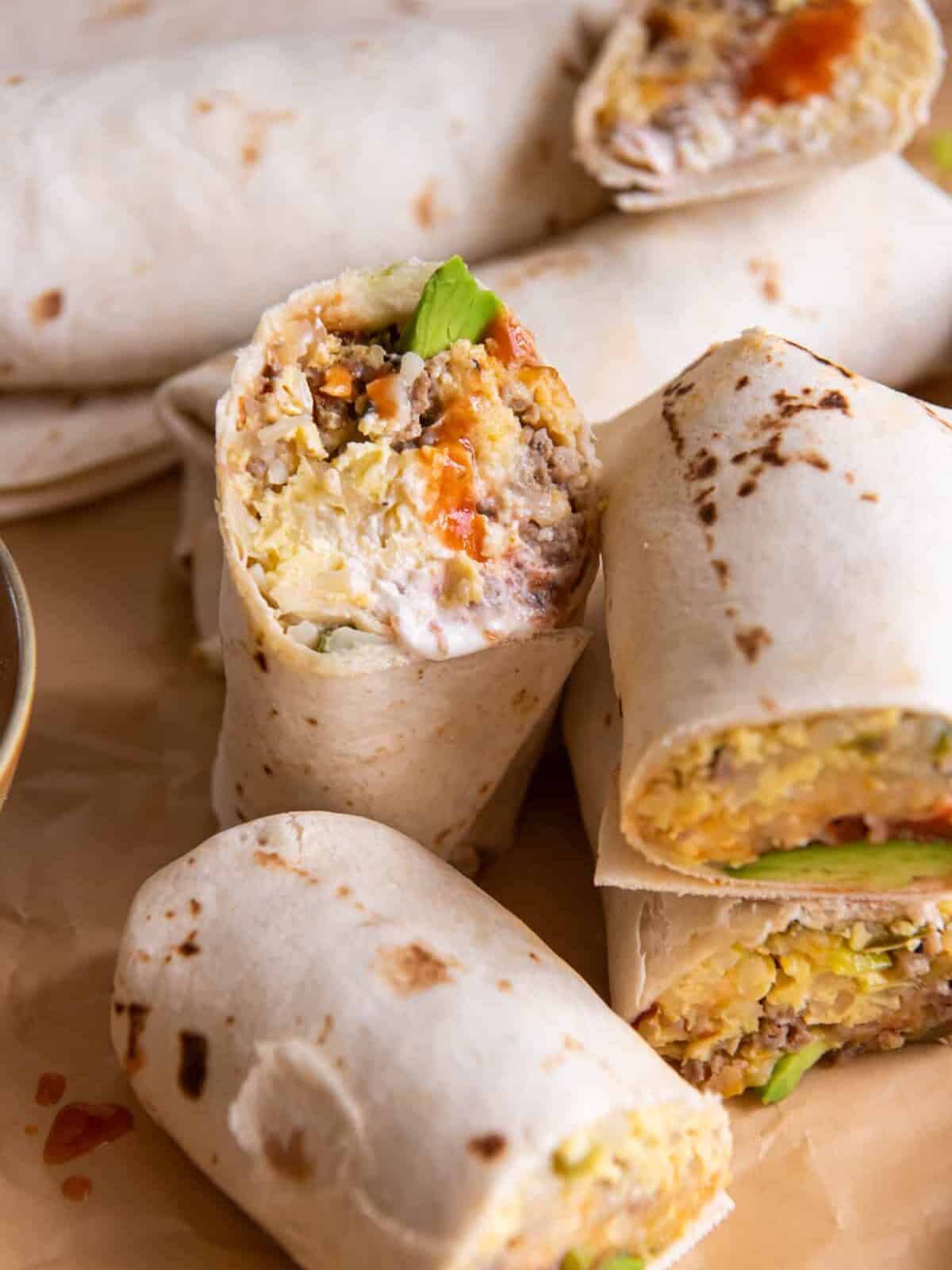 a pile of crockpot breakfast burritos cut in half to reveal the egg and sausage filling