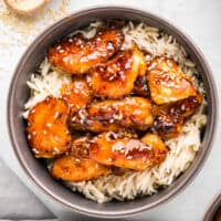 A bowl of asian chicken with rice and sesame seeds.