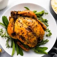 Roasted chicken on a white plate with sprigs of thyme.