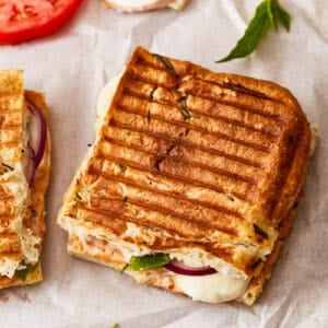 Two grilled sandwiches with tomatoes and onions on a piece of paper.