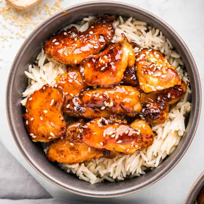 A bowl of sesame chicken with rice and sesame seeds.