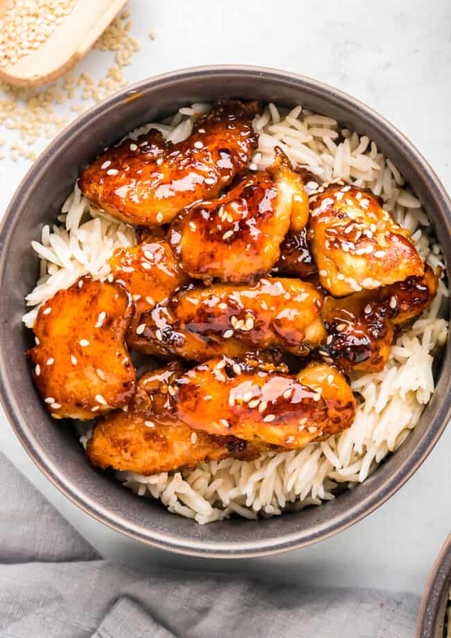 A bowl of sesame chicken with rice and sesame seeds.