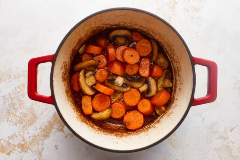 A pot filled with carrots and mushrooms on a white background.