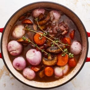 A pot of stew with carrots, onions and mushrooms.