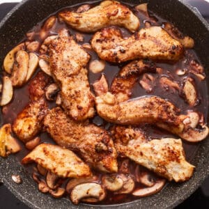 A skillet full of chicken and mushrooms in a sauce.