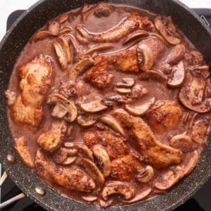 A skillet filled with chicken and mushrooms in a sauce.