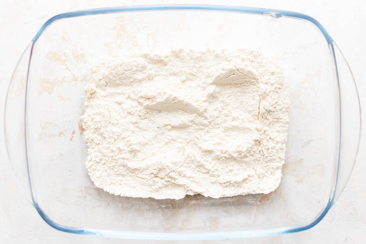 Flour in a glass bowl on a white surface.