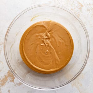 Peanut butter in a glass bowl on a white surface.