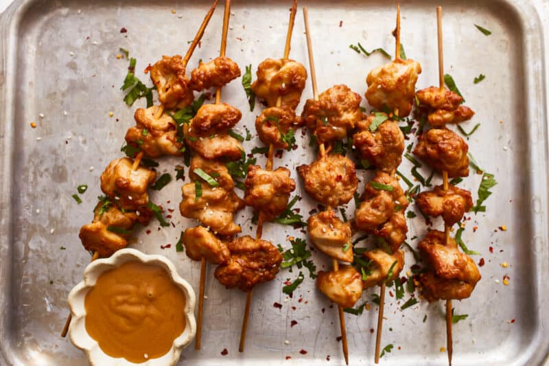 Chicken skewers with sauce on a tray.
