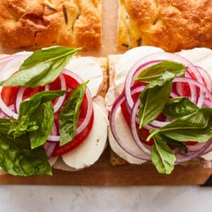 Two sandwiches with tomatoes and onions on a cutting board.