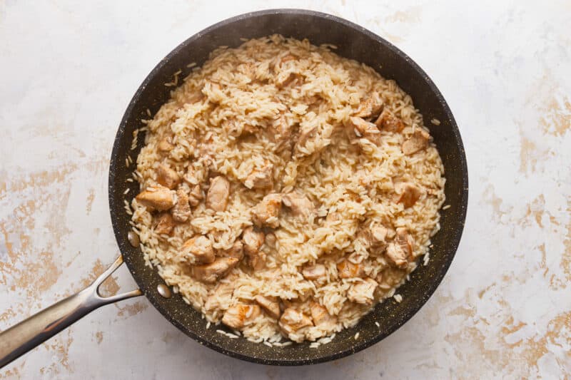 A frying pan with rice and chicken in it.