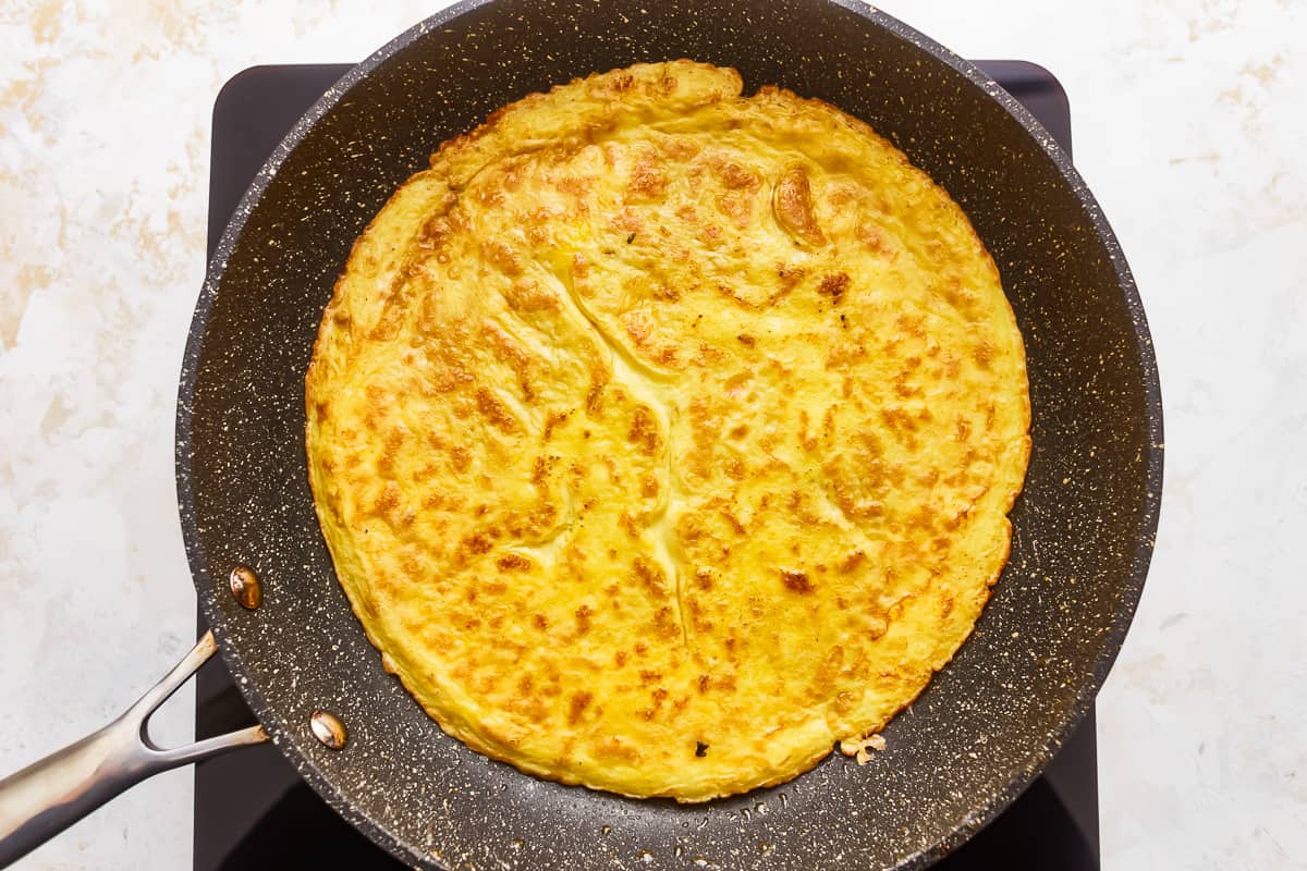 An omelette in a frying pan on a stove top.