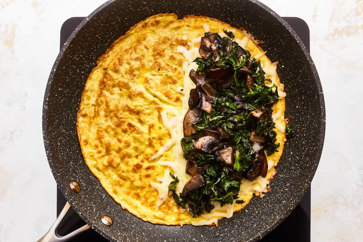 An omelet with mushrooms and kale in a skillet.