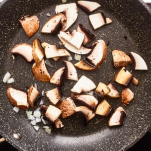Sliced mushrooms in a frying pan on a white background.