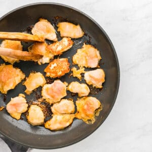Fried chicken in a frying pan with tongs.