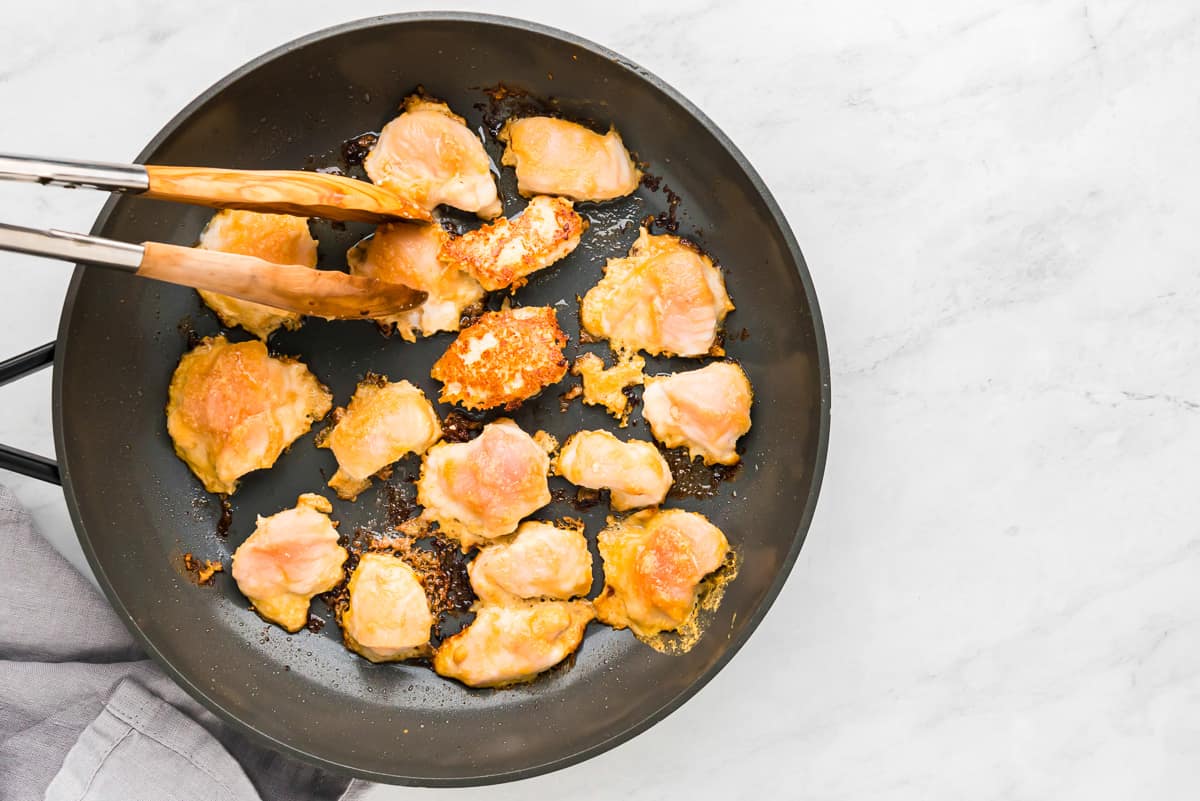 Fried chicken in a frying pan with tongs.