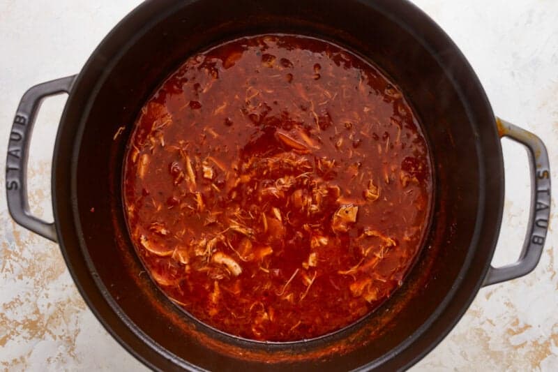 A slow cooker full of sauce with chicken in it.