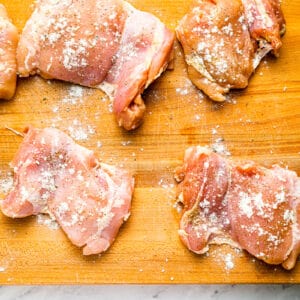 Chicken breasts on a cutting board with salt and pepper.