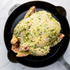 A chicken in a pan with pesto on it.