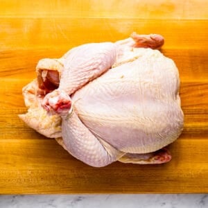 A chicken is sitting on a wooden cutting board.