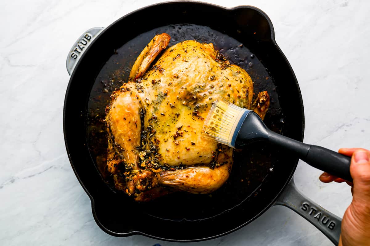 A person is slicing a chicken in a skillet.